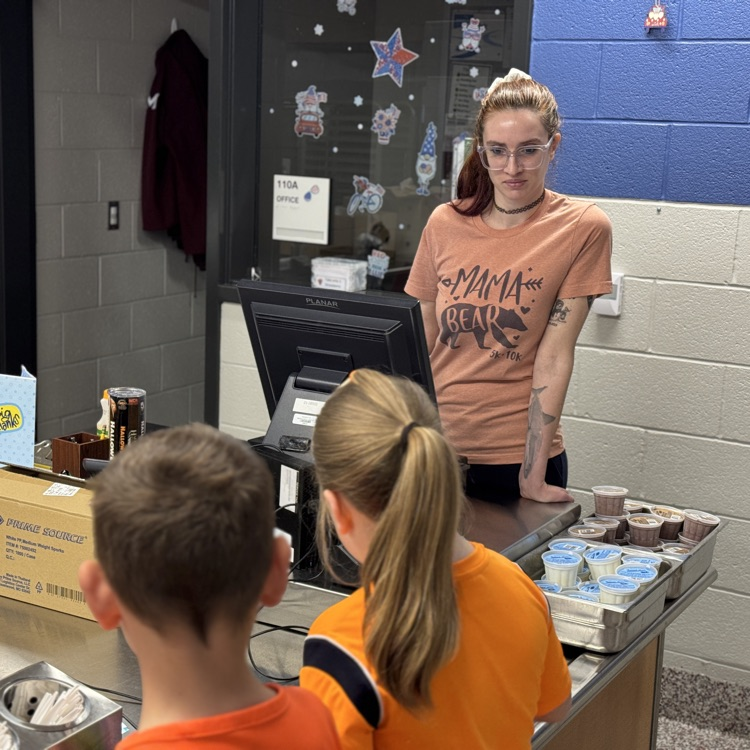 A lady stands behind a register in a school cafeteria line