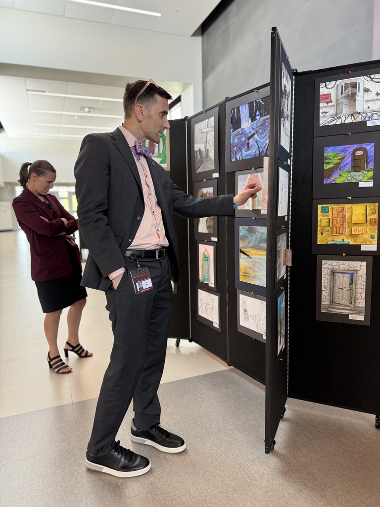 An adult looking at artwork lining a hallway.