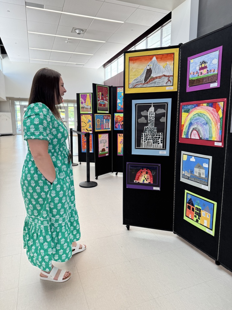 An adult looking at artwork lining a hallway.