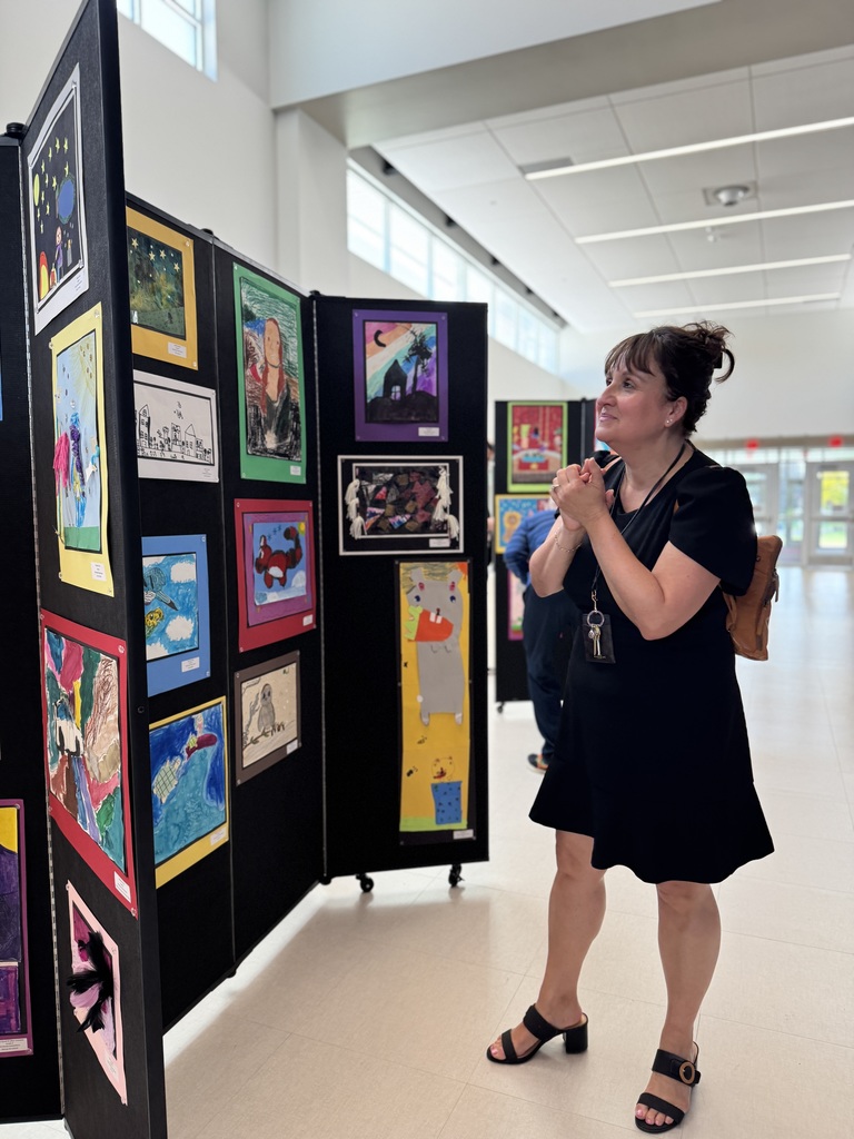 An adult looking at artwork lining a hallway.