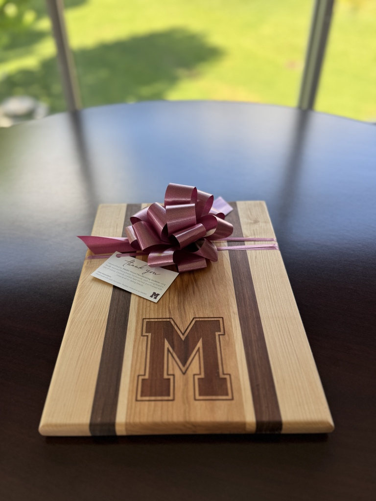 A picture of a handcrafted cutting board with a maroon ribbon around it.