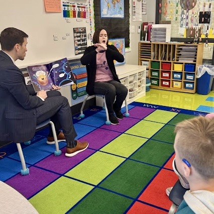 a sign language interpreter signs to a class while an adult reads a book