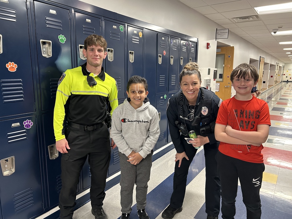 Two police officers stand next to tow students in a school hallway. 