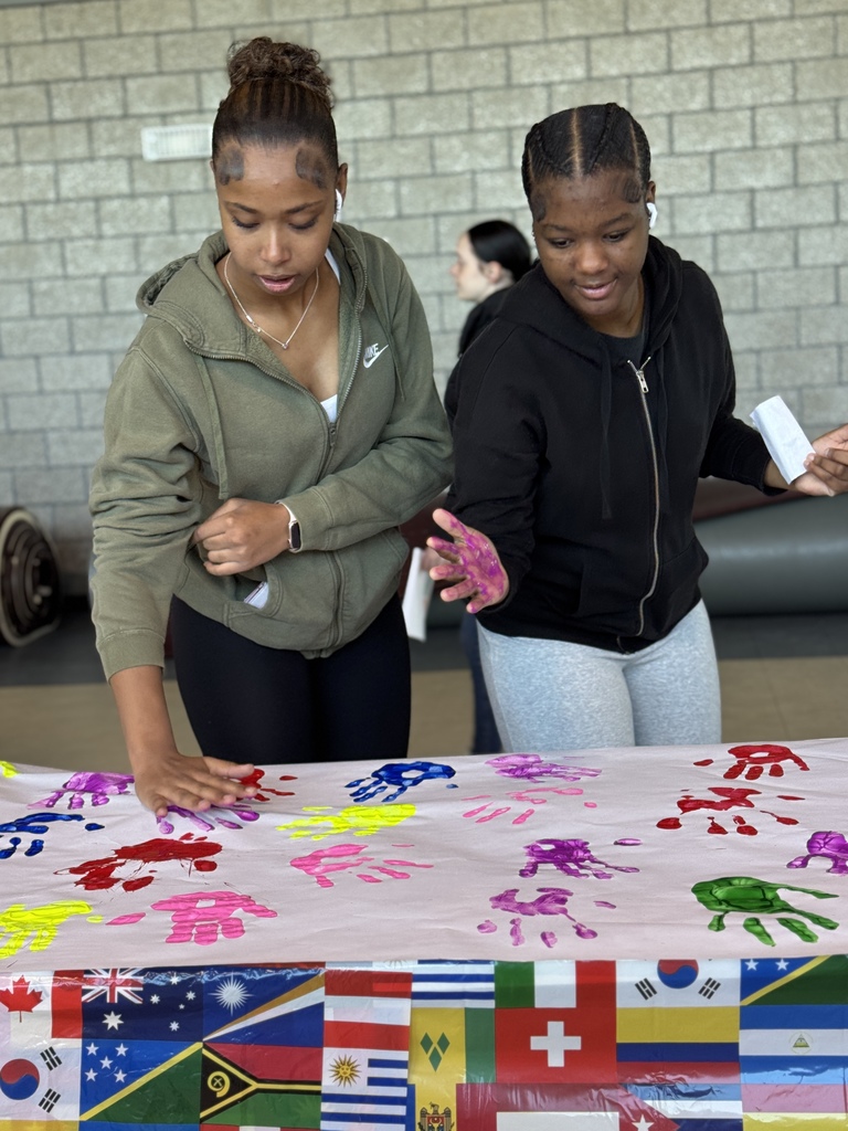 Two students paint their hands to leave a handprint on a colorful canvas.