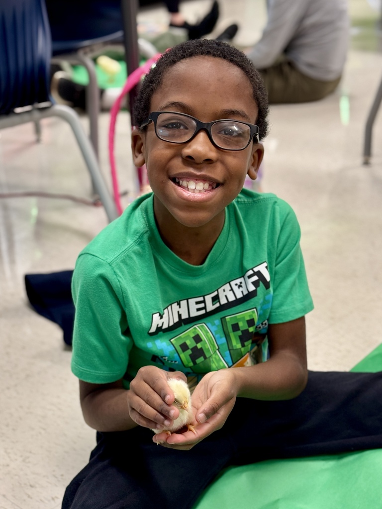 A young student sits on the floor holding a baby chick.