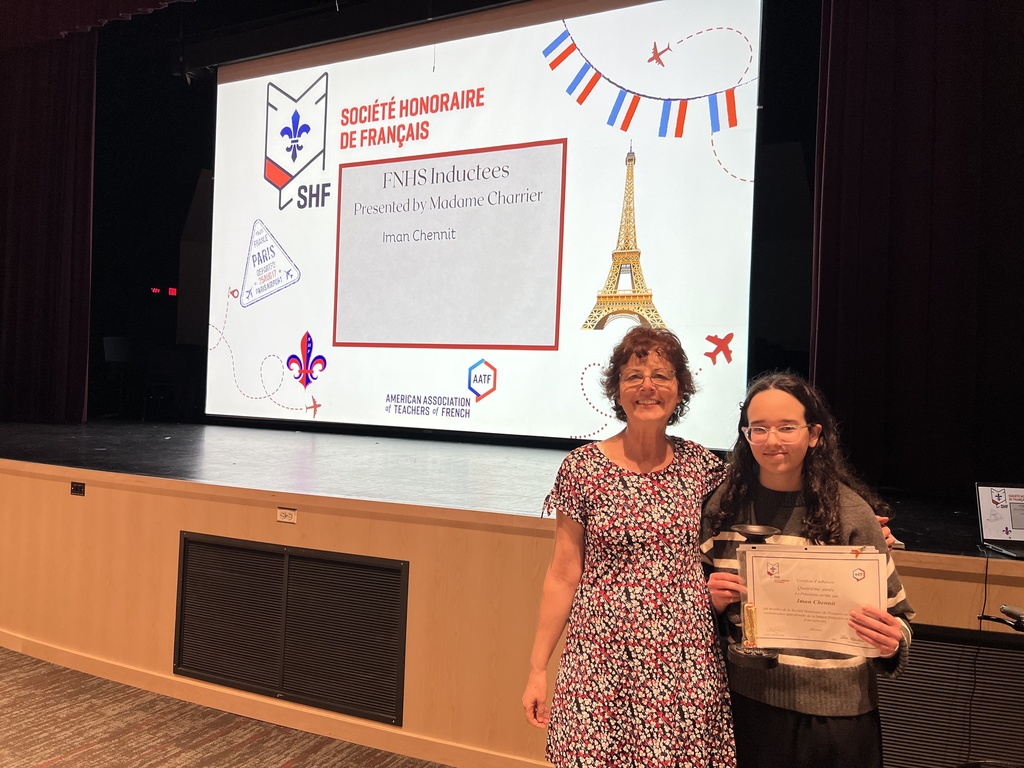 A student standing with a teacher and holding a certificate of assomplishment.