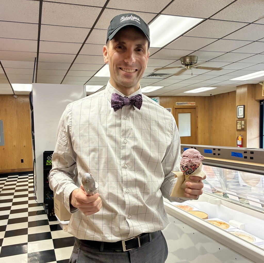A man in a bowtie holds an ice cream scoop and an ice cream cone.
