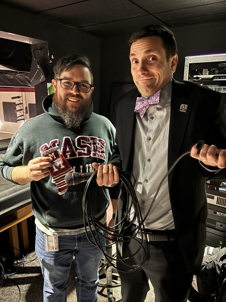 Two men stand side by side, holding socks and a cord, and looking confused.