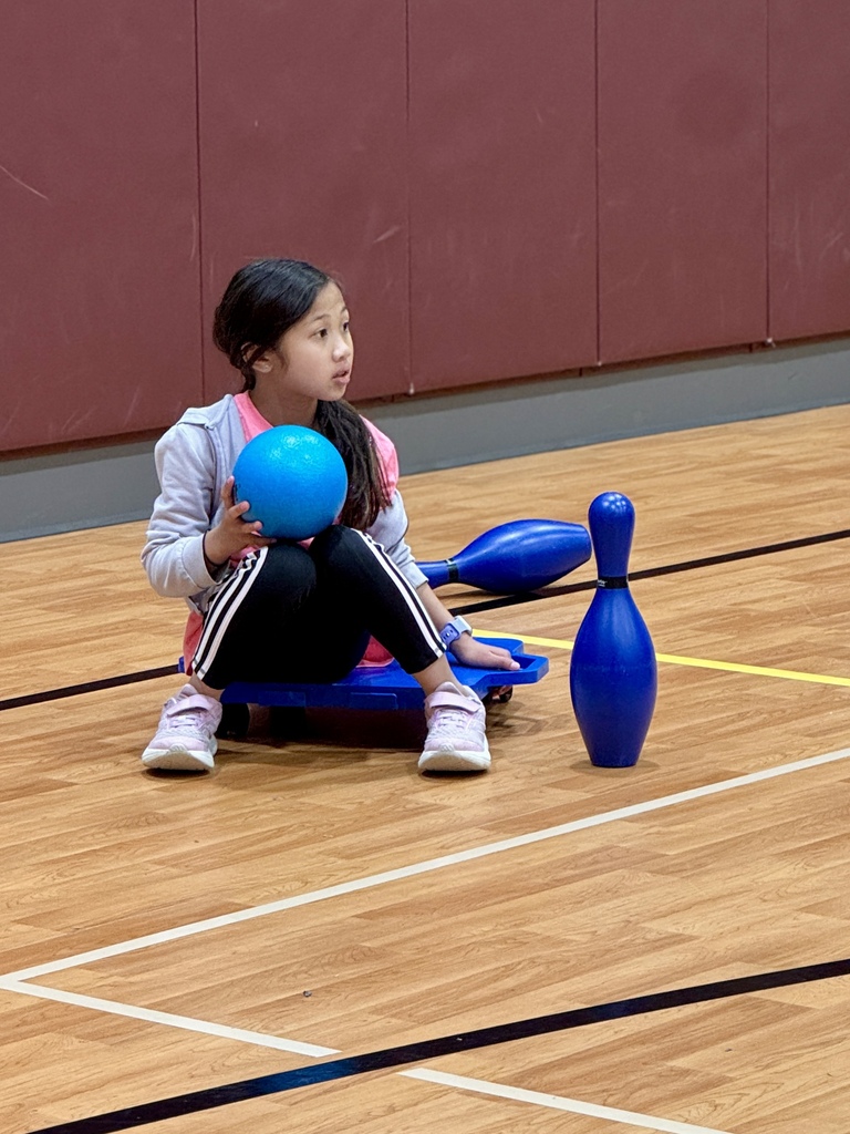 A young girl sits on a scooter while holding a bowling ball.