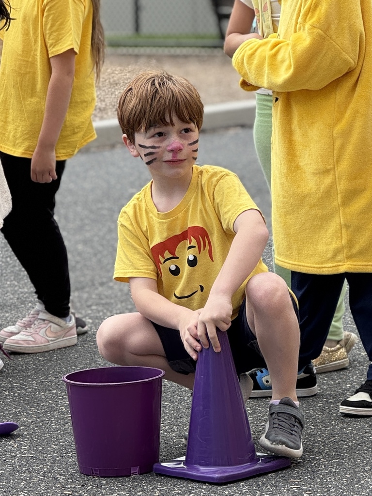 A young student squatting in front of a purple cone and bucket.