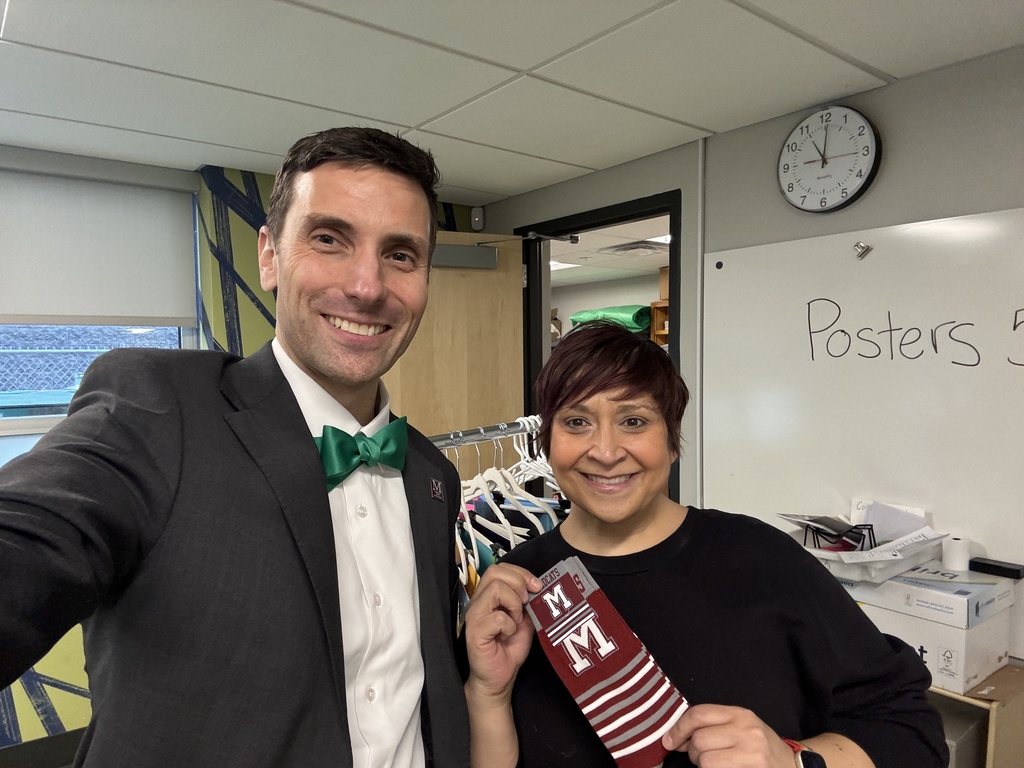 A man in a suit takes a selfie with a woman who is holding a pair of branded M socks.