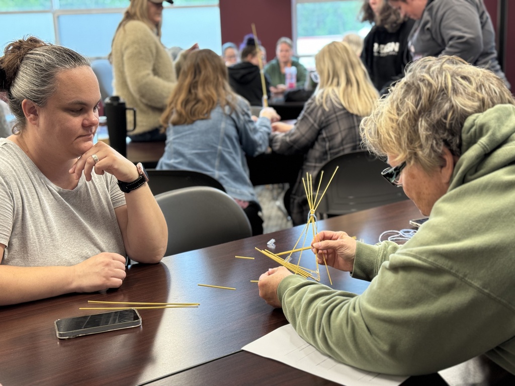 A group of adults around a table working together to build the tallest tower with random supplies.
