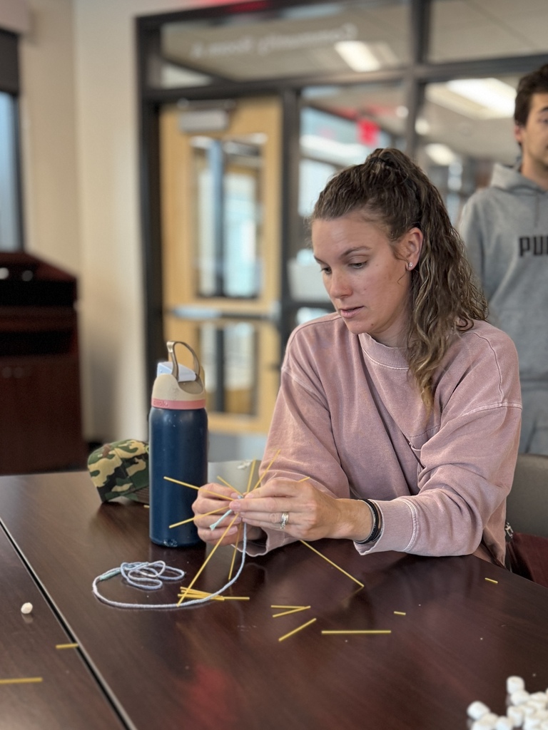 An adult around a table working together to build the tallest tower with random supplies.