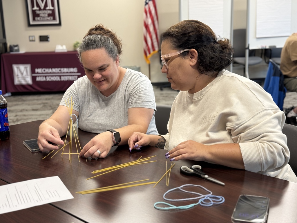 A group of adults around a table working together to build the tallest tower with random supplies.
