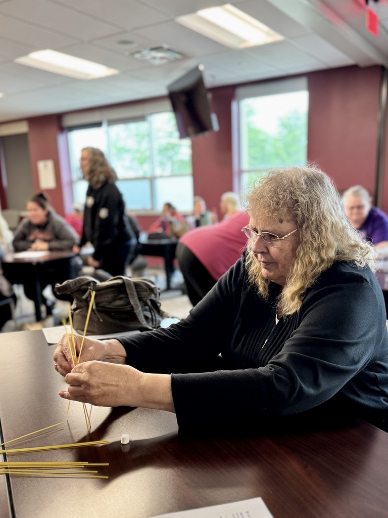 An adult around a table working together to build the tallest tower with random supplies.