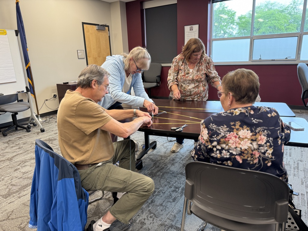 A group of adults around a table working together to build the tallest tower with random supplies.