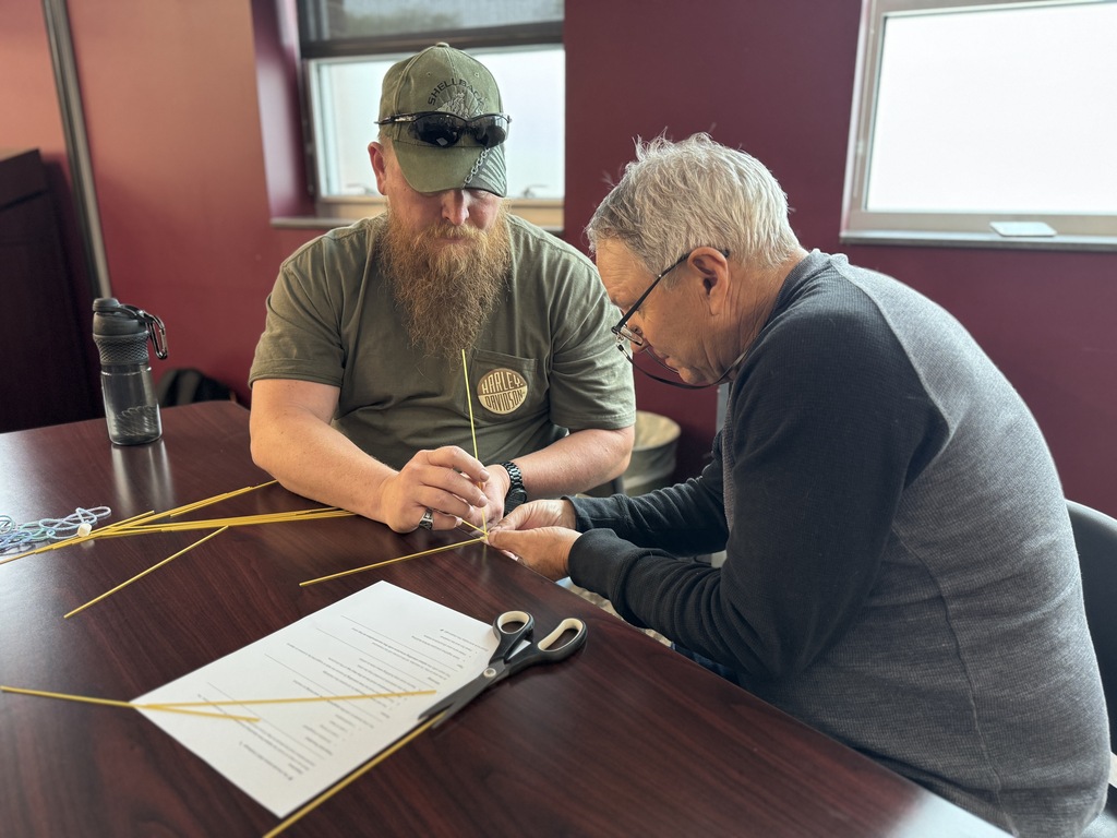 A group of adults around a table working together to build the tallest tower with random supplies.