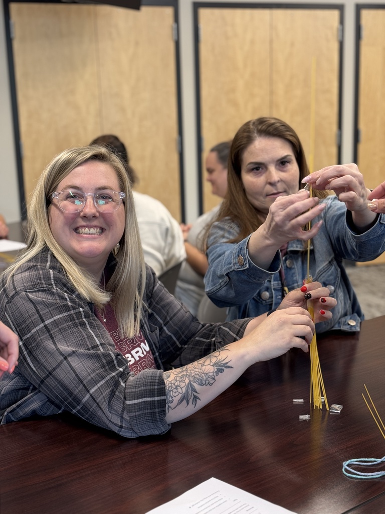 A group of adults around a table working together to build the tallest tower with random supplies.