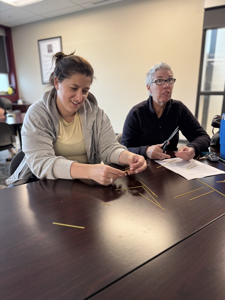 A group of adults around a table working together to build the tallest tower with random supplies.