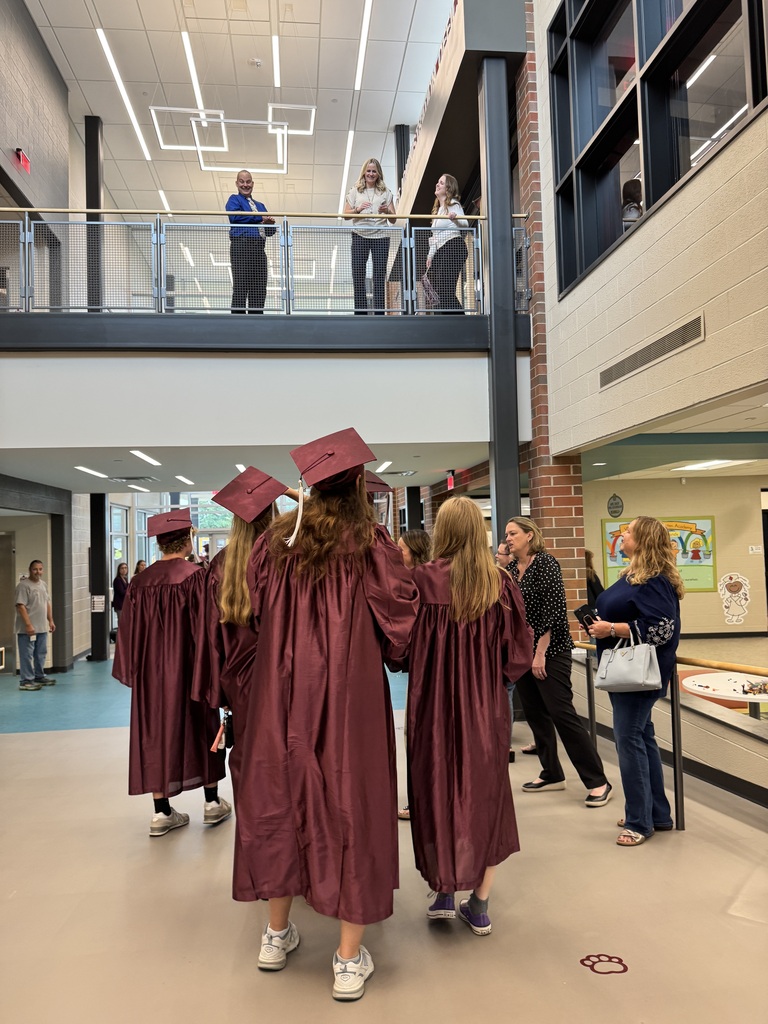 Staff stand on a catwalk to look down and cheer on graduates in caps and gowns.