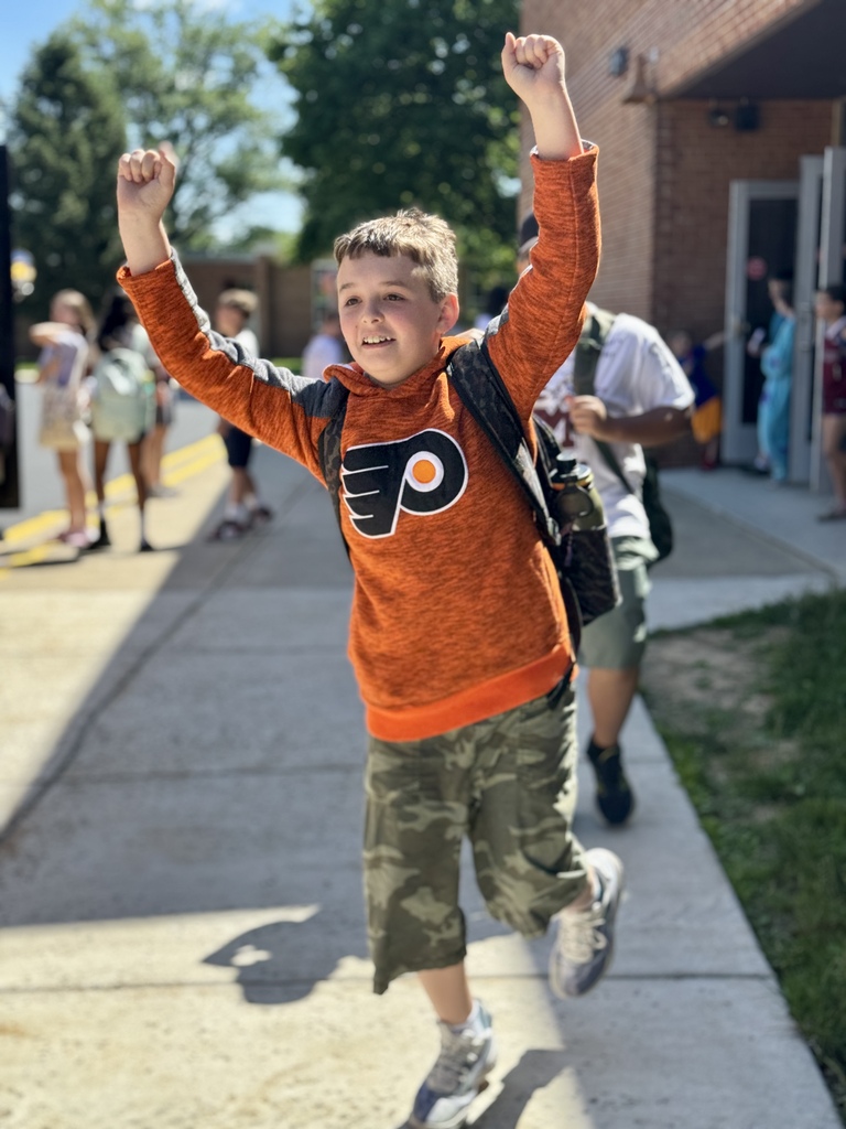 A student runs out of school on the last day, hands in the air and big smile on his face.