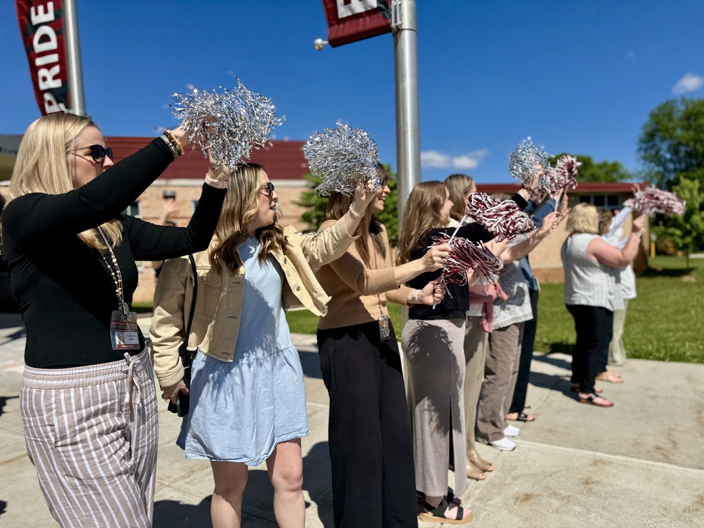 Staff with pom poms cheer and wave goodbye on the last day of school.