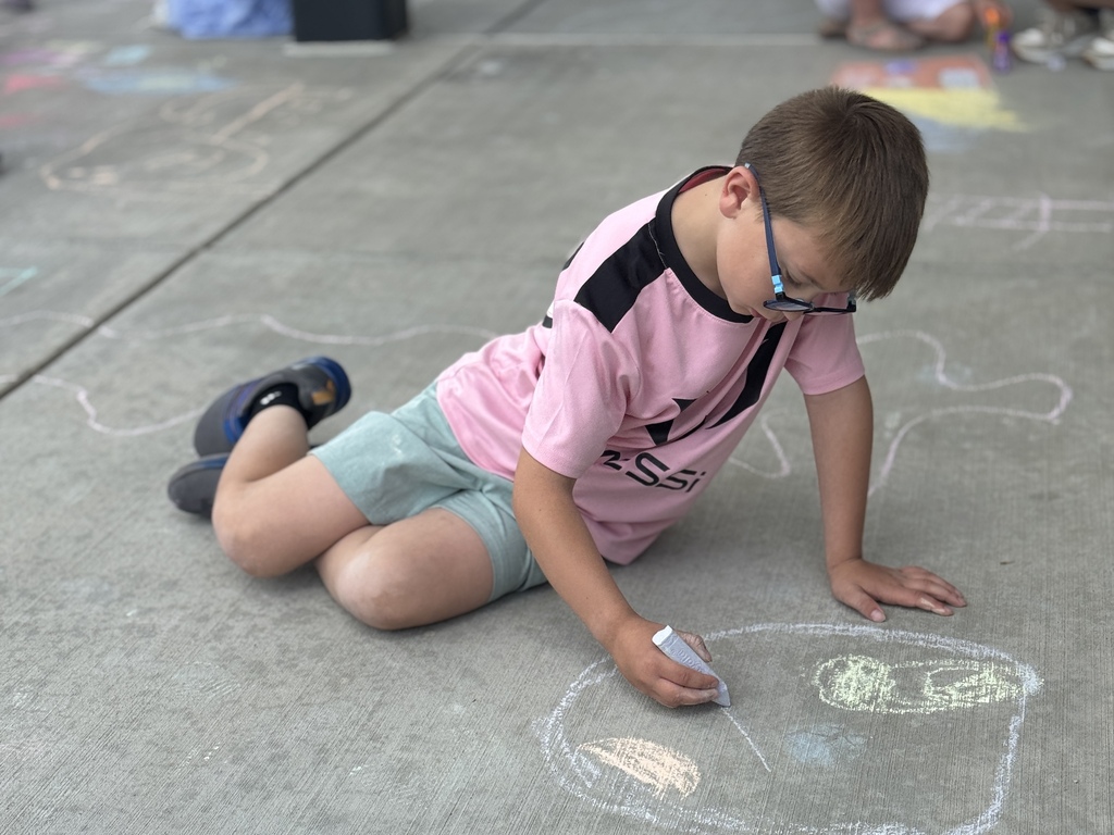 A young boy draws on a sidewalk with chalk.