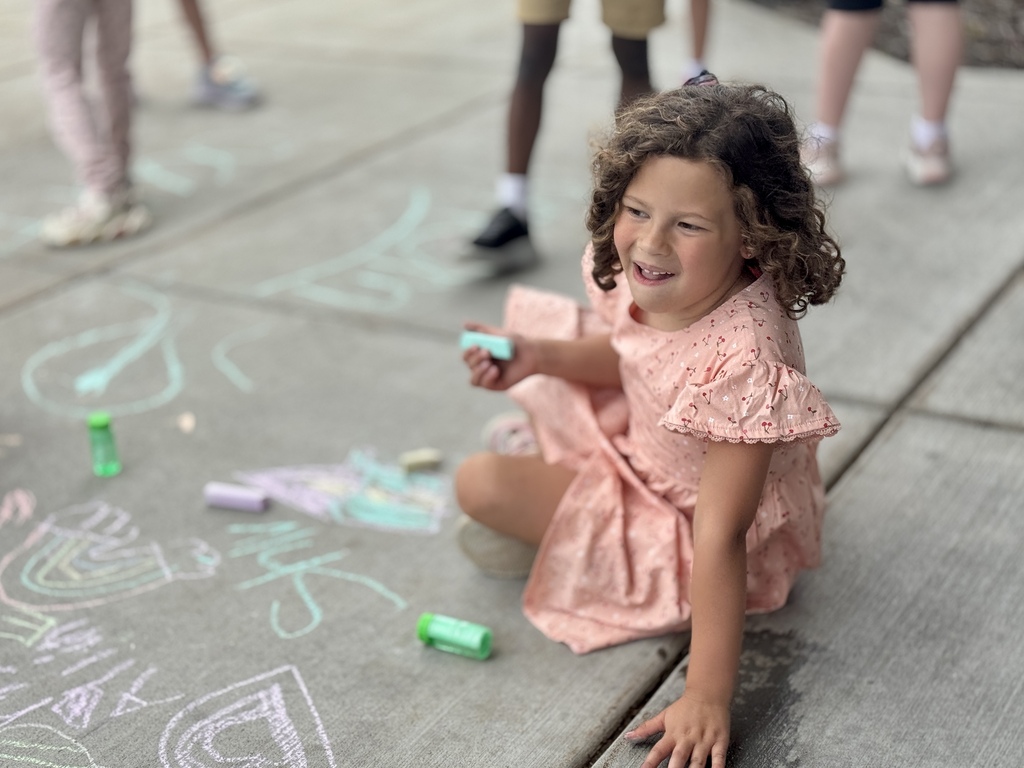 A young girl draws on the sidewalk with chalk.