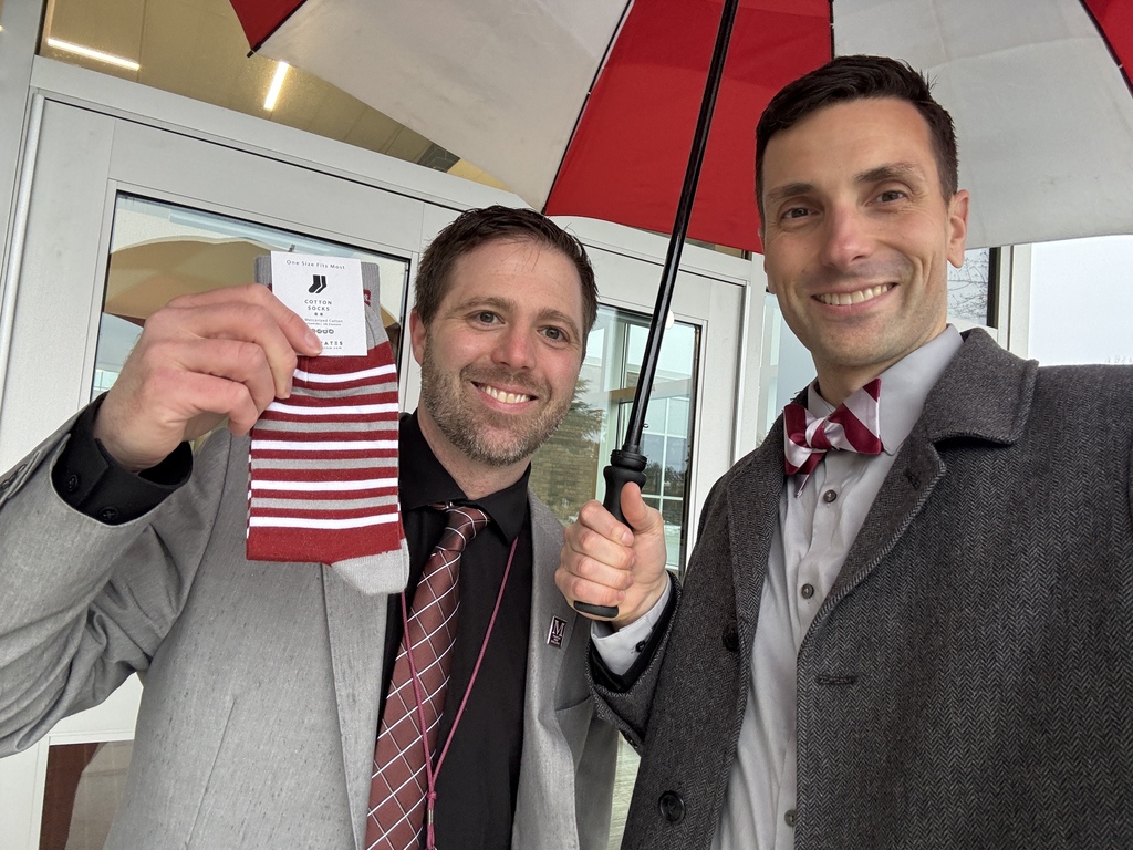 Two men in suits huddled under an umbrella, one holding a pair of branded socks.