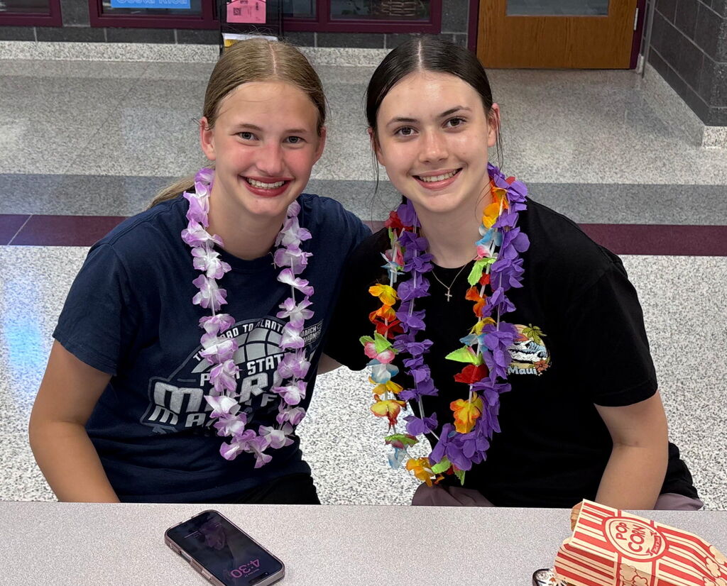 Two students sitting side by side wearing a hawaiian lei.