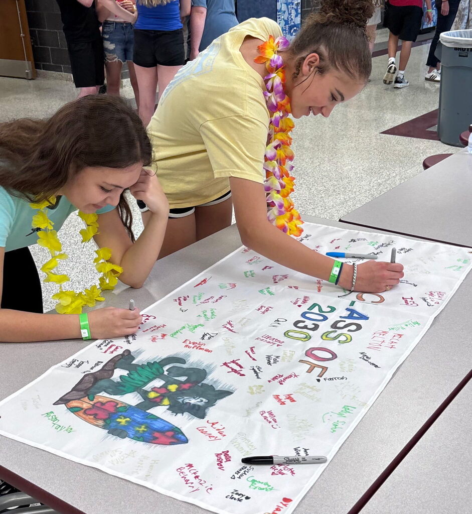 Two students sign a banner.