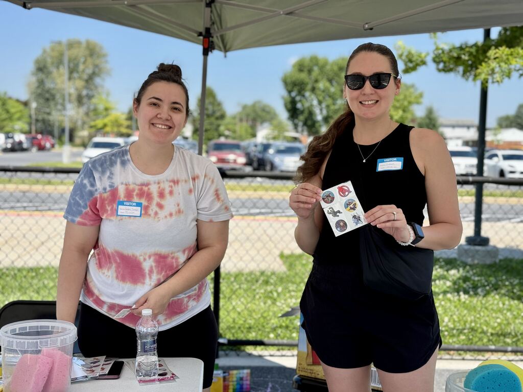 Two adult volunteers stand at a table holding temporary tattoos.