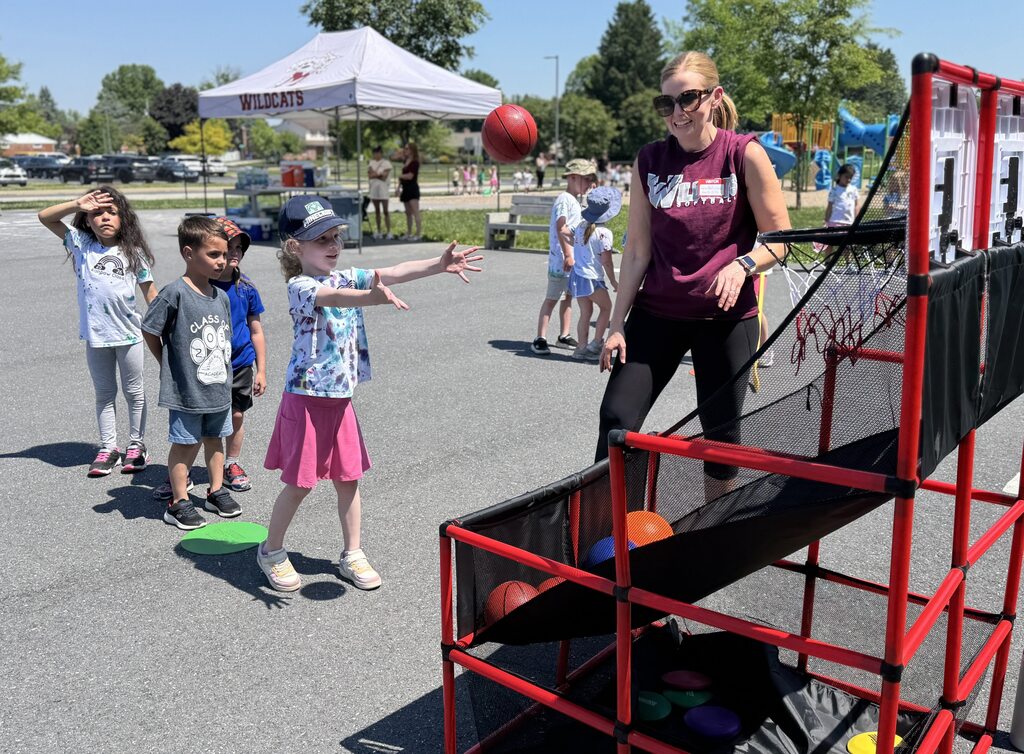 An adult volunteers at a basketball game for young children.