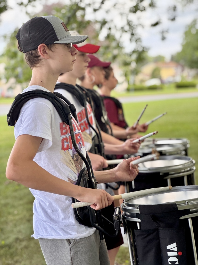 Students stand in shade and practice playing drums.