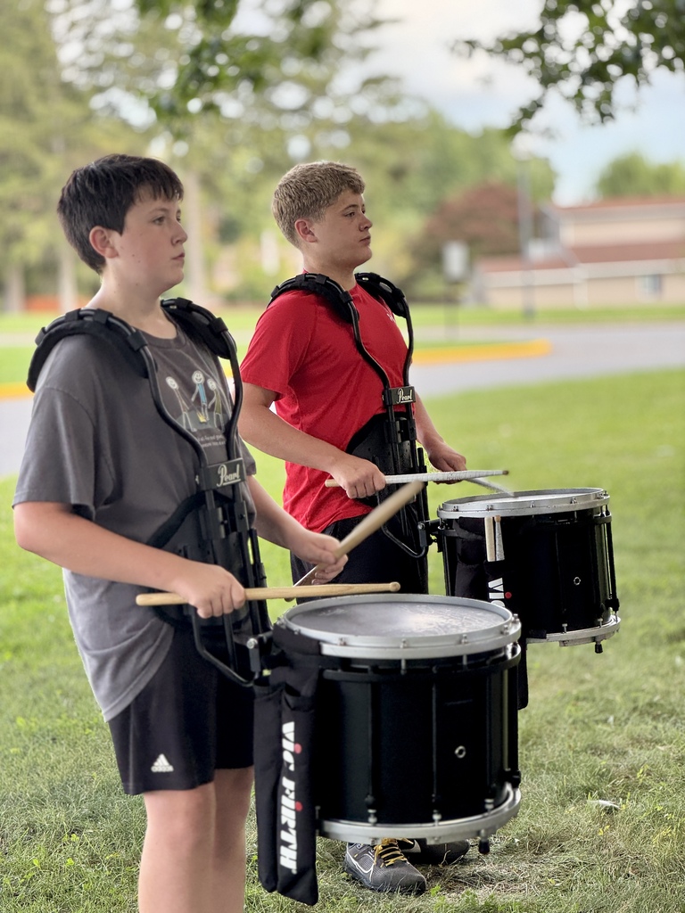 Students stand in shade and practice playing drums.