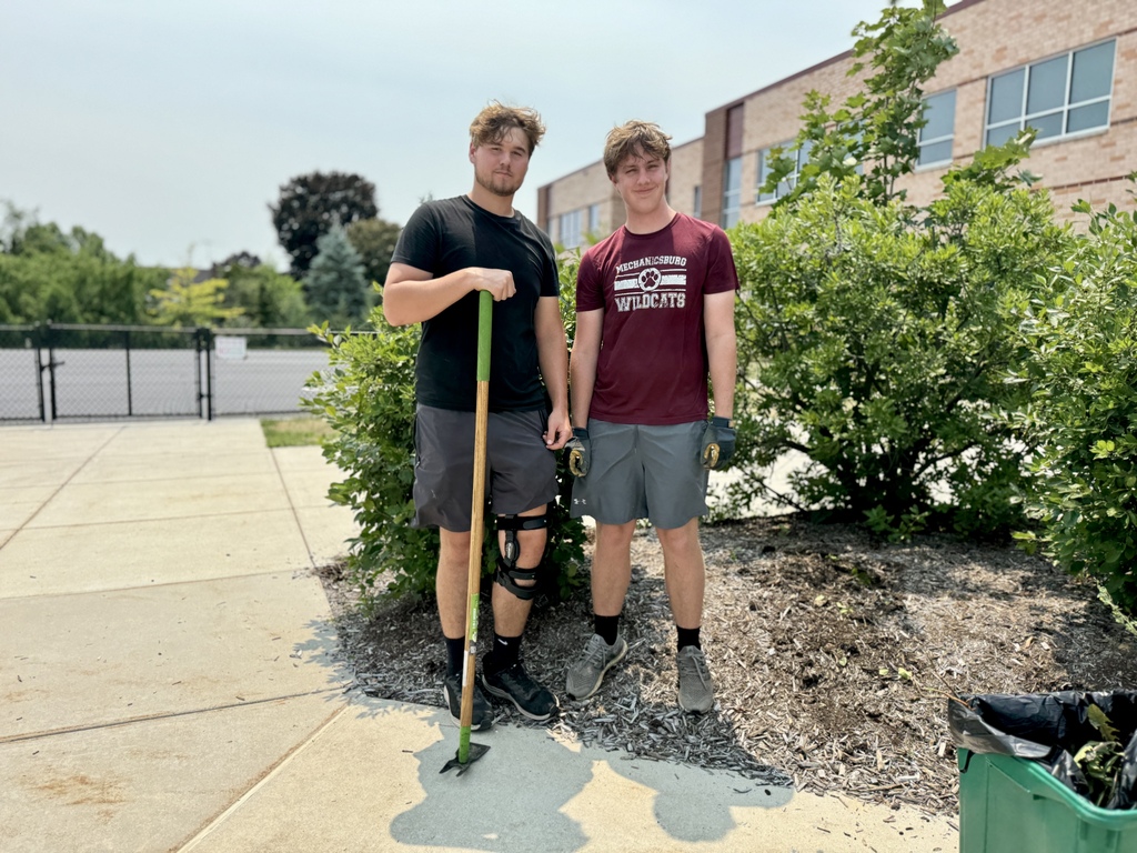 Two young men standing in a flower bed to do some landscaping.