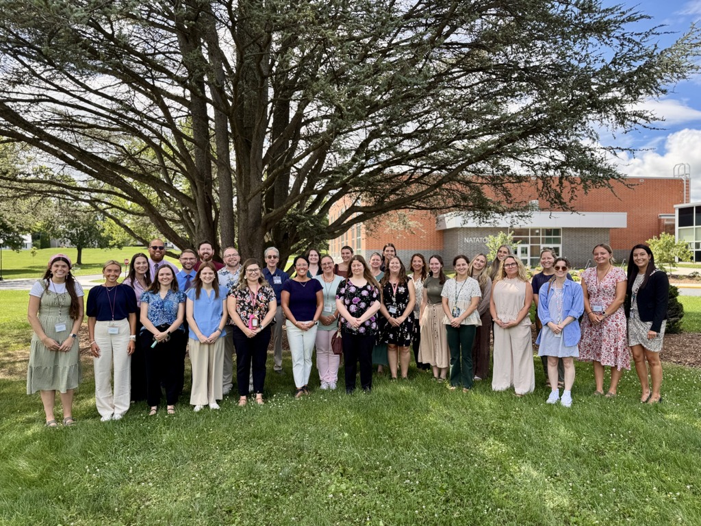 A group of staff members standing under a shaded tree in front of a school building.
