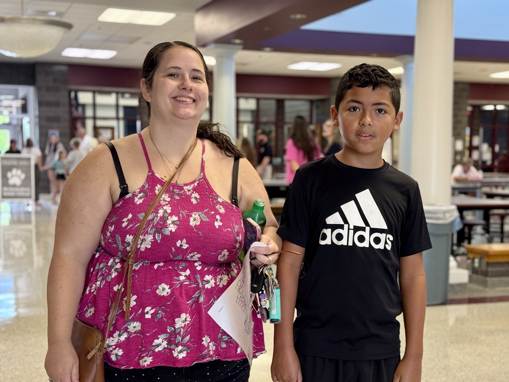 A proud mom stands next to her son at a school.