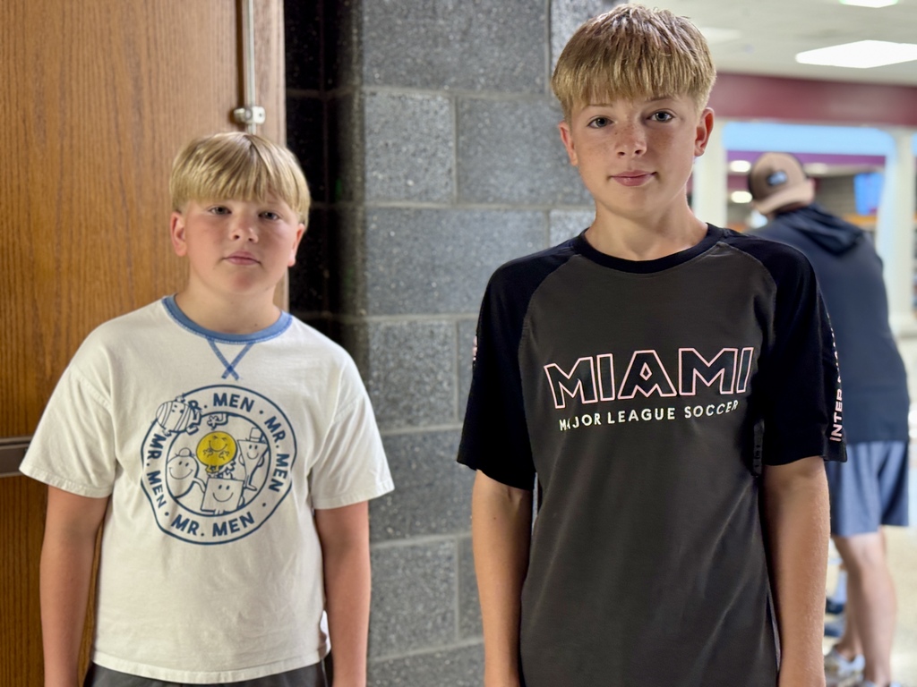 Two young boys stand together in a hallway.