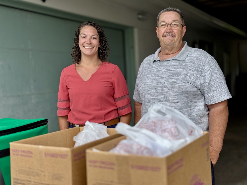 A man and woman standing in front of a box packed with food donations.