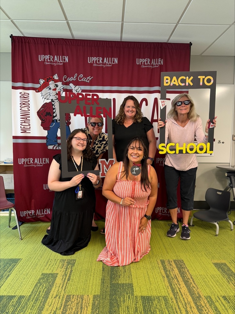 Teachers standing in front of a banner and holding photo props.