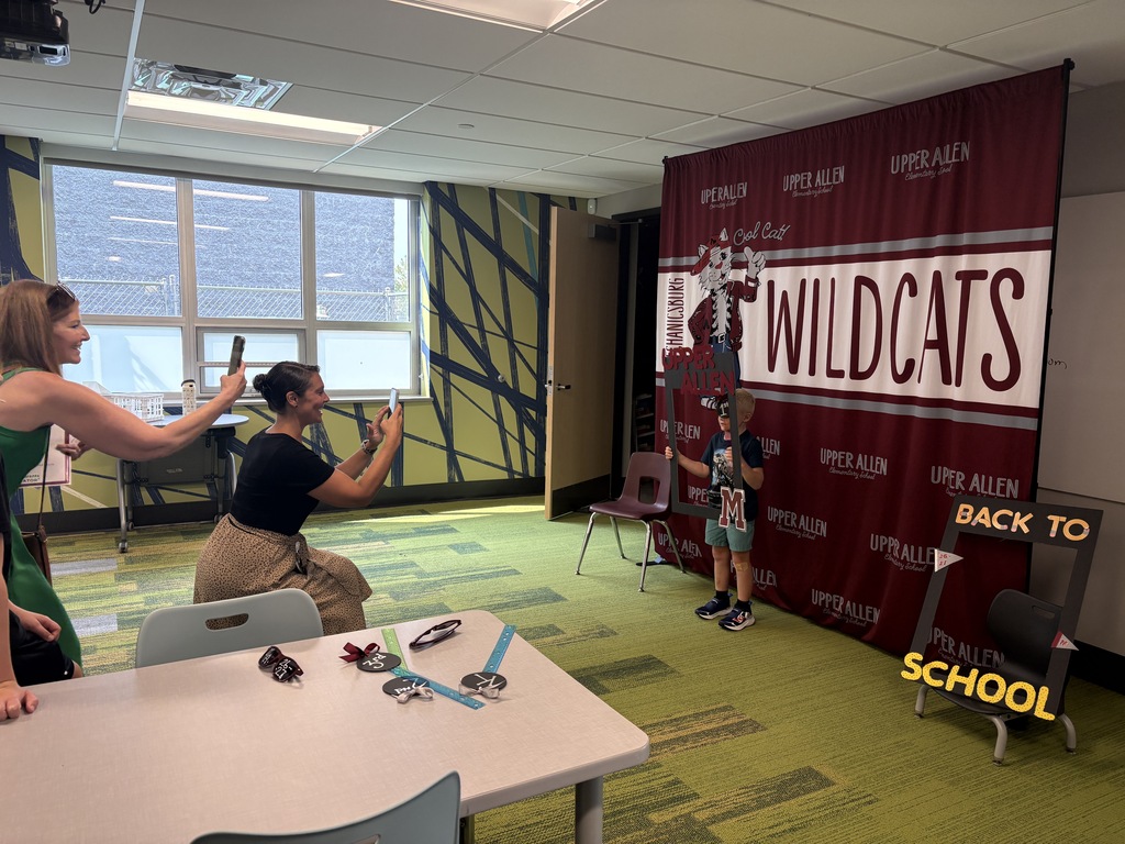 Adults taking a photo of a young student standing in front of a banner with props.