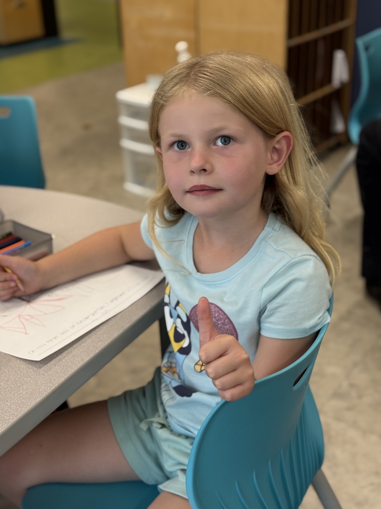 A young girl smiles and gives a thumbs up.