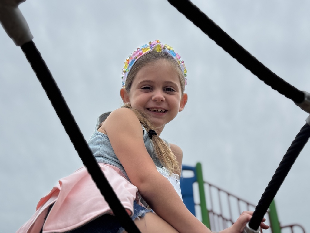 A girl climbs the spiderweb at a school playgorund.