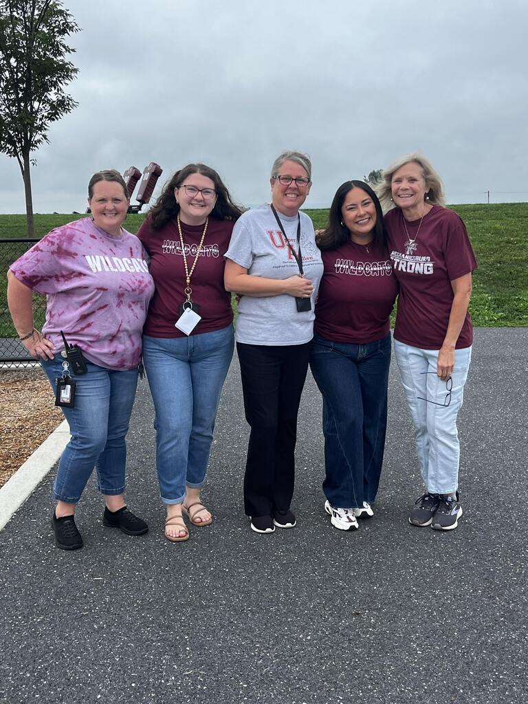 Adults standing arm in arm, showing off their maroon and steel colored shirts.