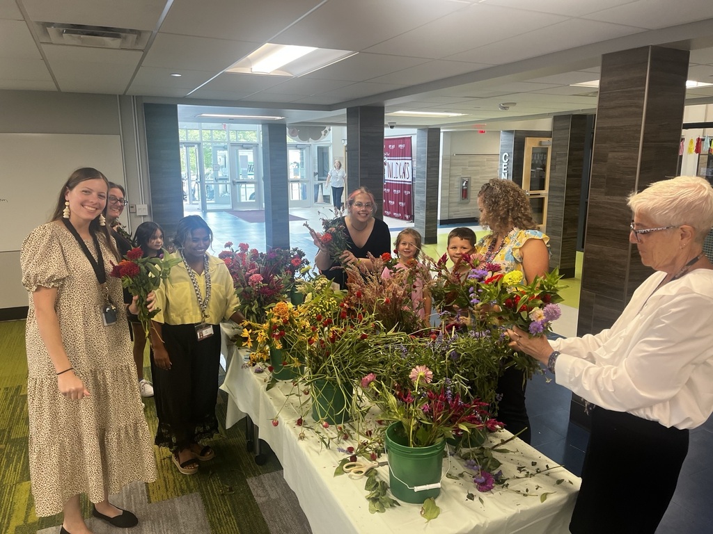 Students and staff stand around a table of fresh cut flowers.