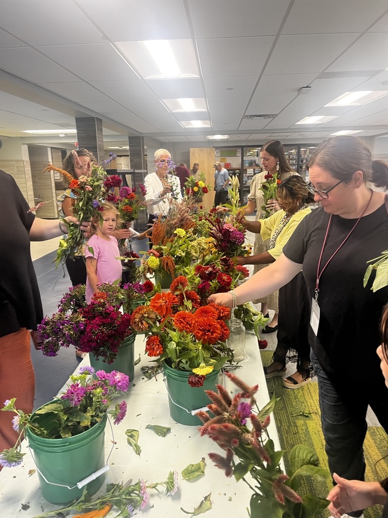 Students and staff stand around a table of fresh cut flowers.