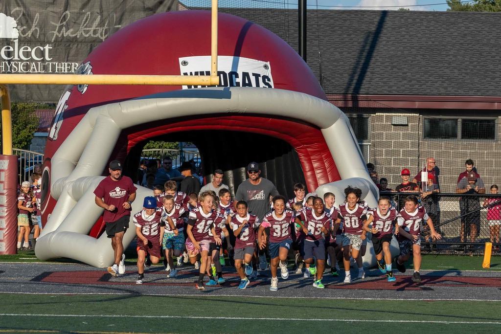 Young football players run out of a blow up helmet.