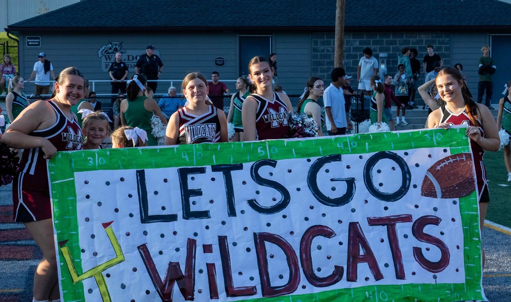 Cheerleaders in front of a Let's Go Wildcats banner.