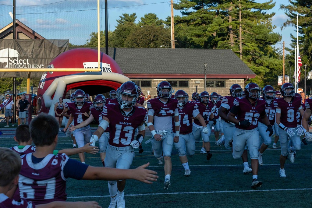 Football players run onto the field and are greeted by younger players.
